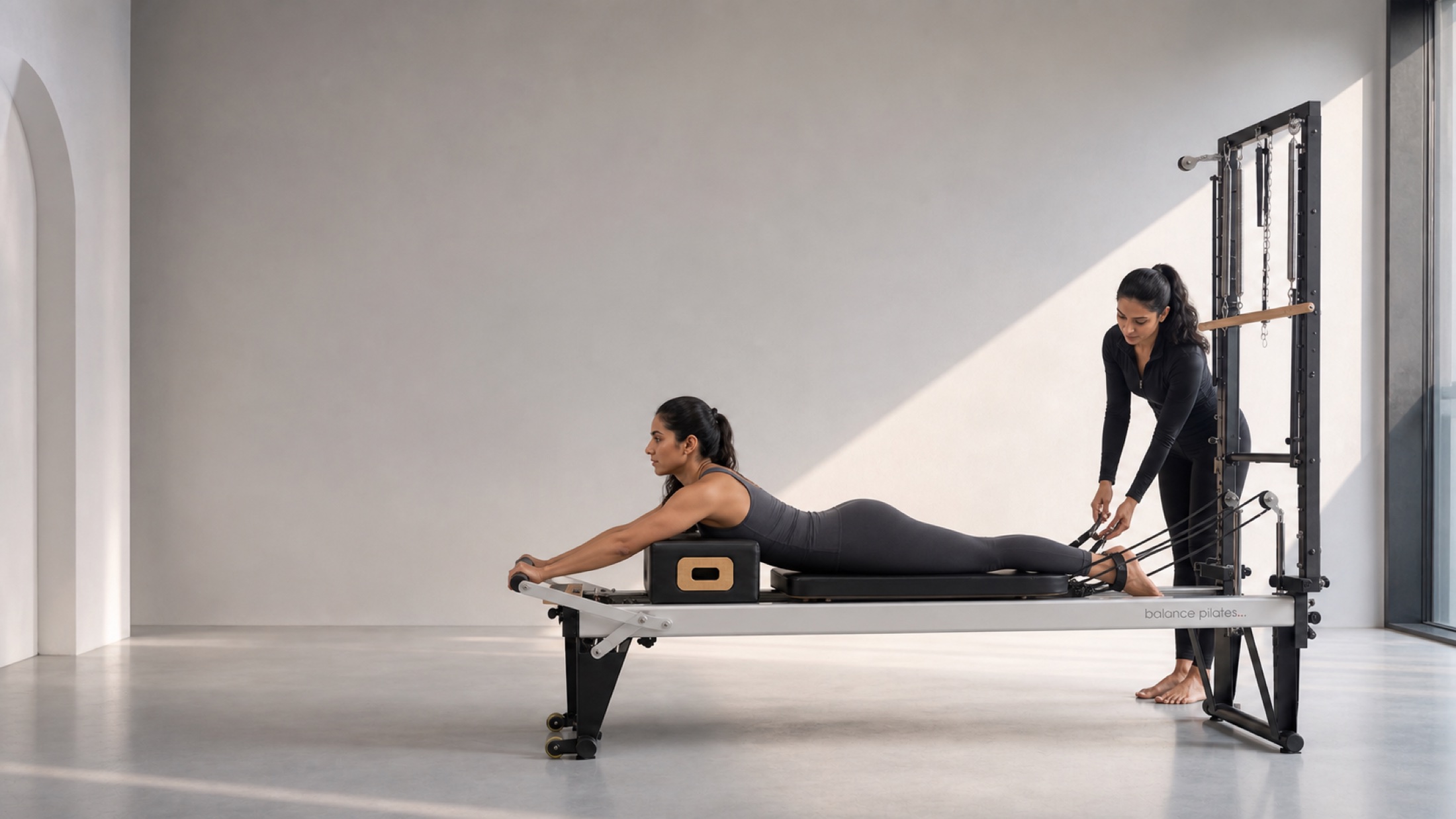 Physiotherapist in black supervising a client on Reformer and Cadillac equipment